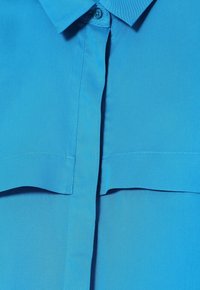 Lyseblå skjorte med krave, knaplukning og brystlomme. Glat, let struktureret stof med en pæn finish.