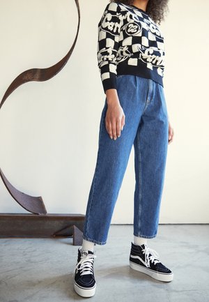 Un pull à motifs noir et blanc avec des carreaux et du texte, associé à un jean en denim bleu taille haute et des baskets montantes noires.