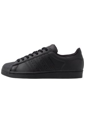 Baskets Adidas Superstar en cuir noir avec un embout en caoutchouc, des bandes texturées, des lacets plats et un col rembourré. Surface lisse, design bas.