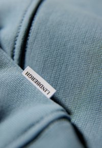 Tela azul texturizada con un patrón tejido, presentando una etiqueta blanca visible con "Lundbergh" impresa en negro. Vista en primer plano del material.