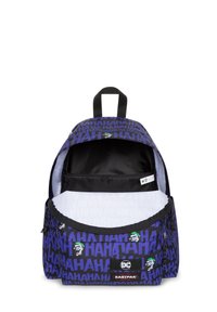 Mochila de tela púrpura con patrón negro de "JA JA JA", que cuenta con un bolsillo frontal con cremallera y un compartimento interior. Etiquetada con los logotipos de Eastpak y DC.