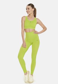 Sutien sport de culoare verde lime și colanți cu talie înaltă, realizați dintr-un material elastic. Prezintă un logo mic pe picior și un design fără cusături.