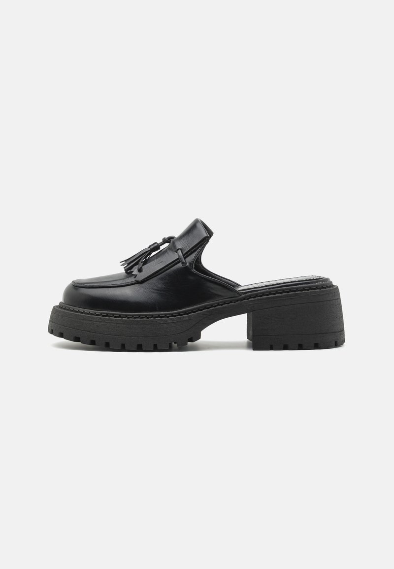 Black leather slip-on shoe with a rounded toe, prominent tassels, a chunky textured sole, and a medium height block heel.