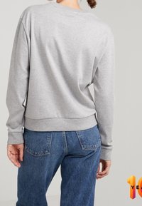 Grijze sweatstof met lange mouwen, geribbelde boorden en zoom, gladde textuur, gecombineerd met blauwe spijkerbroek, gezien vanaf de achterkant.