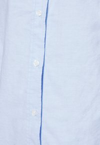 Camicia azzurra chiaro con tessuto a trama, dotata di bottoni bianchi lungo la parte anteriore e di un orlo dritto.