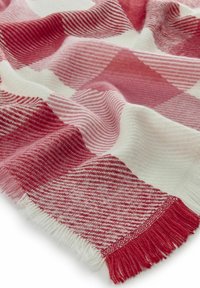 Couverture à carreaux rouge et blanche avec une texture douce, présentant des motifs alternés de rayures et de carrés, finie avec des bords à franges.