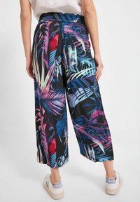 Pantalons évasés en tissu léger avec un motif tropical vibrant et coloré de feuilles sur fond noir.