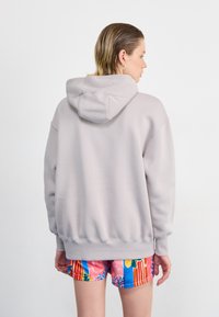 Ljusgrå hoodie med kapuschong, oversized passform, ribbade ärmslut och nederkant. Kombinerad med färgglada, mönstrade shorts med ränder och blommönster.