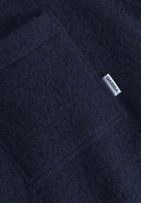 Temno modra flis tkanina z teksturirano površino, ki ima sprednji žep in majhno belo oznako z napisom "GABBA" izšito na njej.