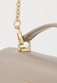 Beige textured handbag with a gold chain strap, featuring a metal clasp and a smooth handle. The surface has a subtle pattern.