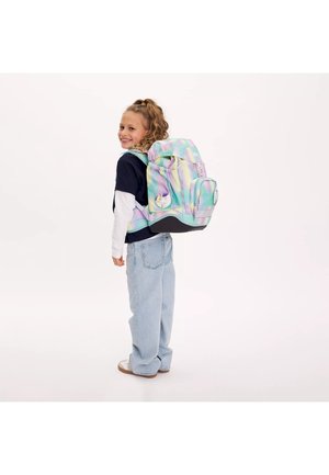 Smiling child wearing light blue jeans, navy and white shirt, carrying a large pastel rainbow backpack with unicorn patches.