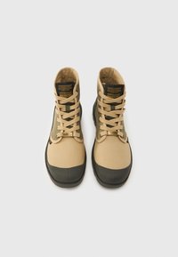 Ζευγάρι από μπεζ και ελιά κορδονιαστά μποτάκια με μαύρες σόλες και ετικέτες "Stranger Things" στη γλώσσα, εμφανιζόμενα από πάνω σε λευκό φόντο.