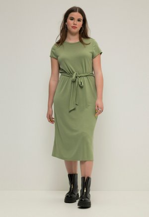 Knee-length, short-sleeve, olive green dress with a belted waist. Paired with black, chunky zip-up boots. Smooth fabric, relaxed fit.