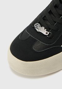 Sorte sneakers med en teksturert overdel og lærdetaljer, en sølvlogo på tungen, og en teksturert kremfarget såle.