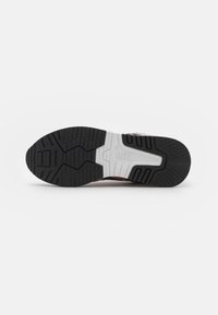 Suola di scarpa sportiva caratterizzata da una robusta costruzione in gomma, pattern di battistrada nero testurizzato e un accento in bianco sulla mescola.