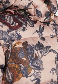 Chaqueta acolchada en rosa suave con estampados botánicos y de animales oscuros, que cuenta con botones y detalles cosidos. Tejido texturizado para mayor calidez.