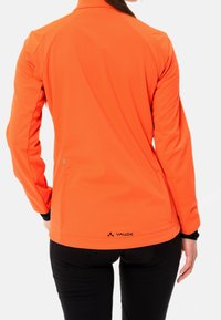 Orange mjukskaljacka med en figursydd design, svarta detaljer vid ärmarna och en logotyp vid nederkanten. Slät textur och lättviktigt material.