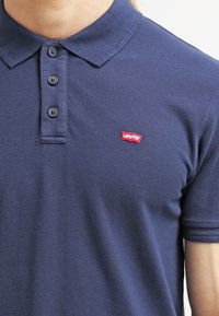 Granatowa koszulka polo wykonana z teksturowanej tkaniny, z trzema guzikami przy zapięciu oraz małym czerwonym logo Levi's po lewej stronie klatki piersiowej.