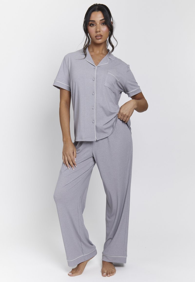 Conjunto de pijama gris que incluye una parte superior de botones de manga corta con un bolsillo y pantalones anchos a juego, acentuados con costuras en blanco. Textura de tela suave.