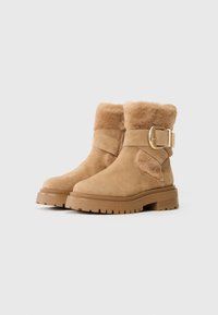 Botas de tobillo de ante color caqui con un suave cuello de piel, que cuentan con un hebilla lateral y una suela de goma gruesa y texturizada.