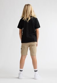 Sort kortærmet t-shirt parret med beige shorts med sidelommer. Hvide sneakers og hvide sokker med striber fuldender outfittet.