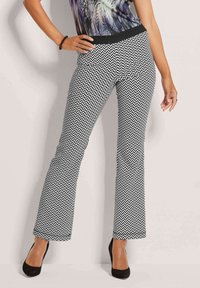 Zwart-witte chevronpatroon flared pants met een rekbare zwarte tailleband, gecombineerd met zwarte hoge hakken.