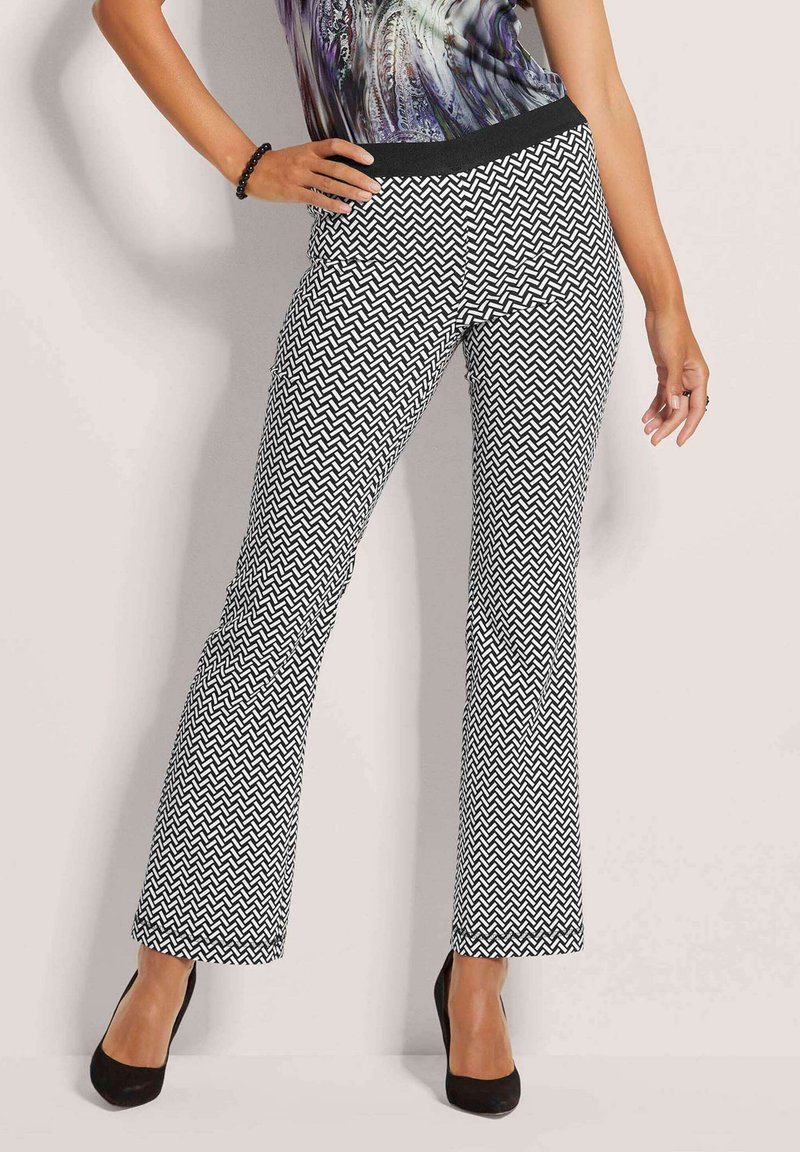 Zwart-witte chevronpatroon flared pants met een rekbare zwarte tailleband, gecombineerd met zwarte hoge hakken.