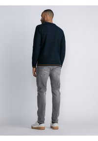 Dunkelblauer gestrickter Pullover mit gerippten Bündchen und Saum, kombiniert mit hellgrauen Jeans und weißen Sneakers mit Gummisohlen. Nur Rückansicht.