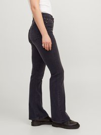Jeans de mezclilla oscuros acampanados con un talle medio, que cuentan con dos bolsillos traseros y herrajes en tono cobre, combinados con botas negras de tobillo.