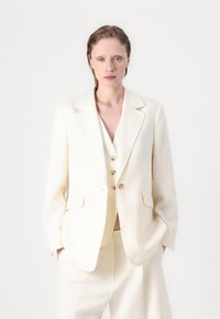 Weißes Blazer mit Reverskragen, zwei Fronttaschen und Drei-Knopf-Verschluss. Über einem passenden Weste und Hose getragen, aus glattem Stoff, lockere Passform.