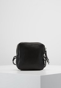 Borsa a tracolla in pelle nera con forma quadrata, chiusura con zip e dettagli con frange laterali. Texture liscia con un design minimalista.
