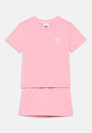 Sada pozostávajúca z ružového rebrovaného trička a sukne, s okrúhlym výstrihom, krátkymi rukávmi a logom Adidas na hrudi a na leme sukne.