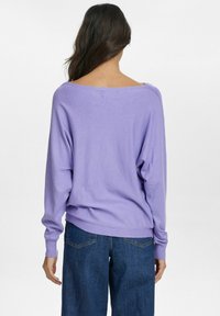Lavendelfärgad oversized tröja med en vid halsringning och långa ärmar, tillverkad av mjukt tyg. Kombinerad med lösa blå denimjeans.