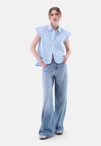 Blusa azzurro chiaro con colletto e maniche corte abbinata a jeans azzurro chiaro a gamba larga. Tessuto liscio, vestibilità comoda e design minimalista.