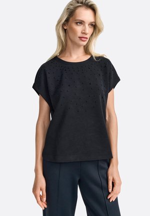 Zwarte top met korte mouwen, voorzien van een ronde hals en een voorzijde versierd met kleine zwarte studs, vervaardigd uit zachte, textuurstof.