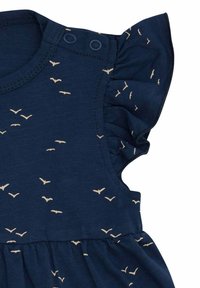 Abito senza maniche di color blu navy con spalline arricciate, caratterizzato da una stampa di uccelli beige sparsi. Due chiusure a scatto sulle spalle. Tessuto morbido.