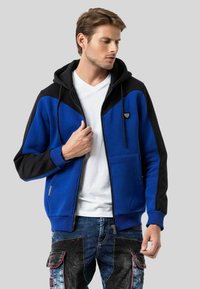 Blau-black zip-up Hoodie mit einer Kapuze mit Kordelzug, Fronttaschen und kontrastierenden Paneelen. Glatte Textur und taillierte Form.