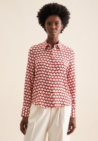 Camicia button-up con un motivo geometrico rosso e bianco, realizzata in tessuto morbido, con colletto classico e maniche lunghe.