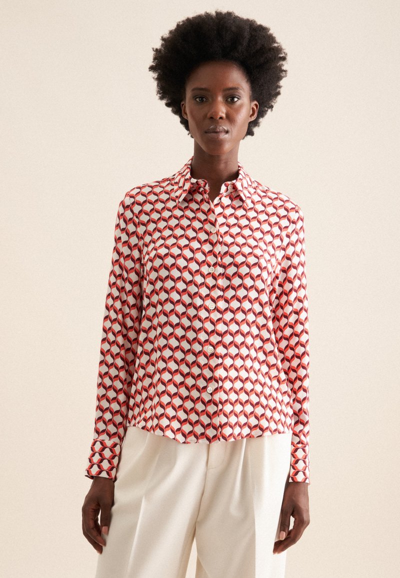 Camicia button-up con un motivo geometrico rosso e bianco, realizzata in tessuto morbido, con colletto classico e maniche lunghe.