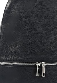 Zwarte leren rugzak met een gestructureerde afwerking, voorzien van een zilveren ritsluiting en twee ritsaanhangers. Rondvorm met gladde randen.