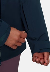 Navy blue jacket with adjustable cuff, featuring a zippered sleeve pocket. Soft fabric, sleek design, and visible stitching detail.