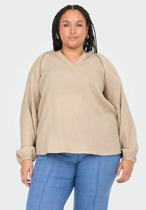 Beige volný top s V-výstřihem, texturovanou tkaninou a dlouhými rukávy s elastickými manžetami, v kombinaci se světle modrými kalhotami rovného střihu.