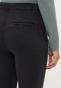 Fekete farmer leggings, karcsúsított fazonnal, sima textúrával, hátsó zsebbel és magas derékkal.