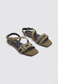 Sandalias planas verdes oliva hechas de ante con múltiples correas con tachuelas, diseño de puntera cuadrada y doble hebilla para ajuste.