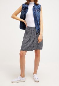 Jeansowa kamizelka na dopasowanym białym topie, w połączeniu z czarno-białą spódnicą w wzory i białymi trampkami. Casualowy styl z luźną sylwetką.