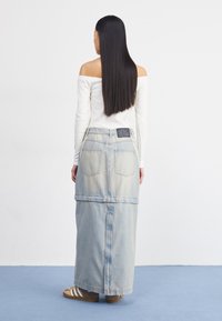 Jupe maxi en denim bleu clair, avec un design superposé. Comprend des poches arrière, un patch en cuir et une section amovible à l'ourlet.
