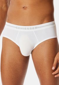 Mannelijk torso in witte Schiesser slips, zichtbaar van taille tot boven de dijen tegen een witte achtergrond.