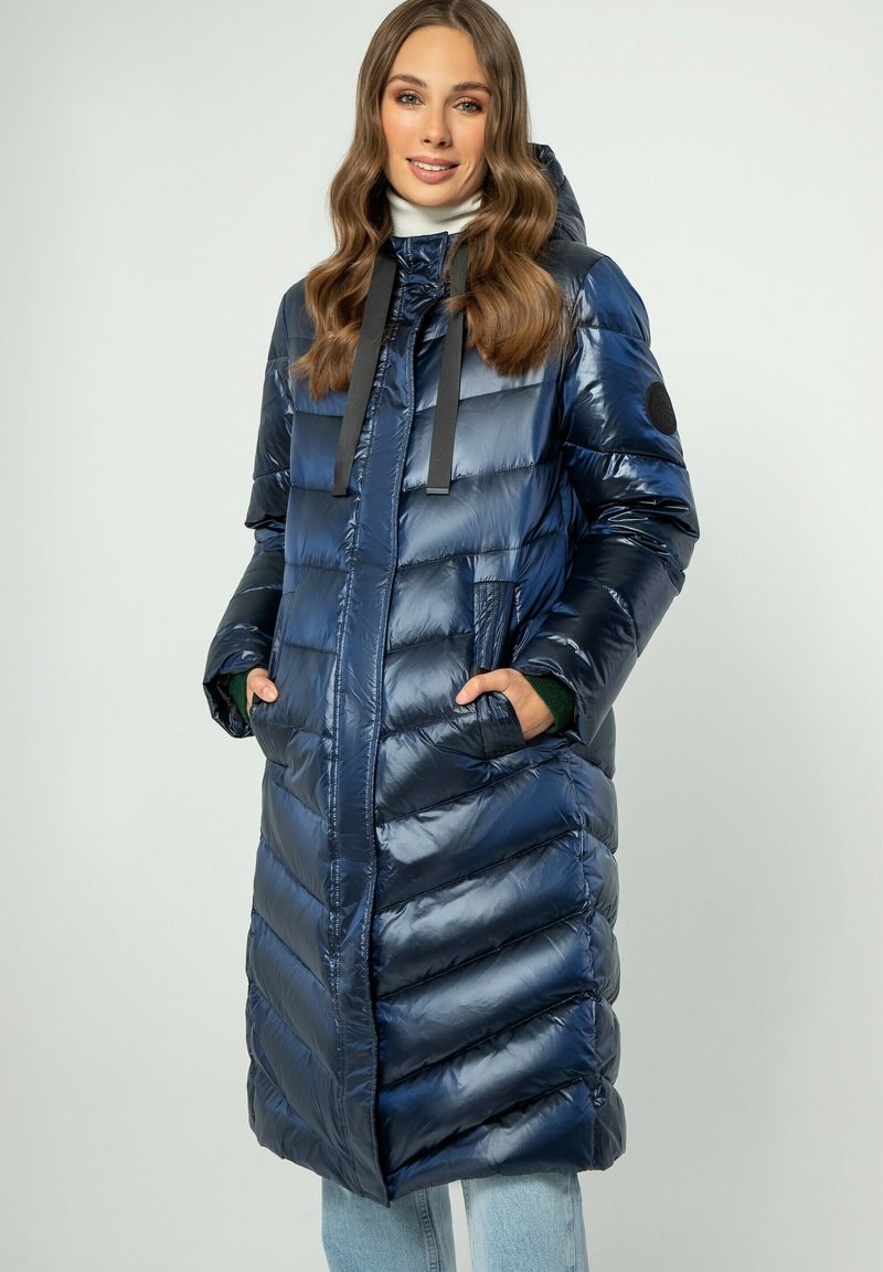 Giacca puffer blu navy con cappuccio arricciato, maniche lunghe, cuciture a zig zag e tasche frontali. Tessuto lucido con dettagli neri.