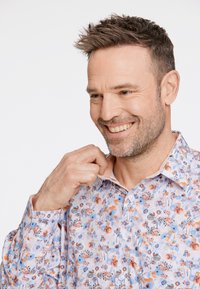 Chemise florale sur un fond clair, présentant des motifs bleus, orange et gris. Conception à boutons, col pointu et boutons visibles.