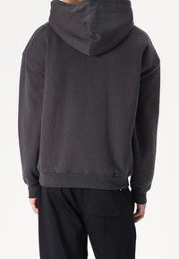 Hoodie in donkergrijs katoen, met een losse pasvorm, ribgebreide manchetten en een onafgewerkte zoom. De achterkant heeft een gladde textuur met minimale naden.